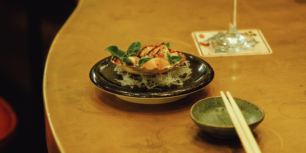 Bossa Nova Sushi in Melbourne, featuring a sleek brass sushi train, warm ambient lighting, with diners enjoying premium Japanese dishes on rotating plates such as scallops.