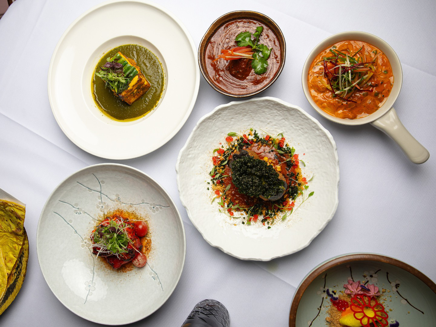 Modern Indian dishes at Atta Melbourne displayed overhead featuring colourful curries, seared fish with roe, vibrant vegetarian plates and a decorative dess