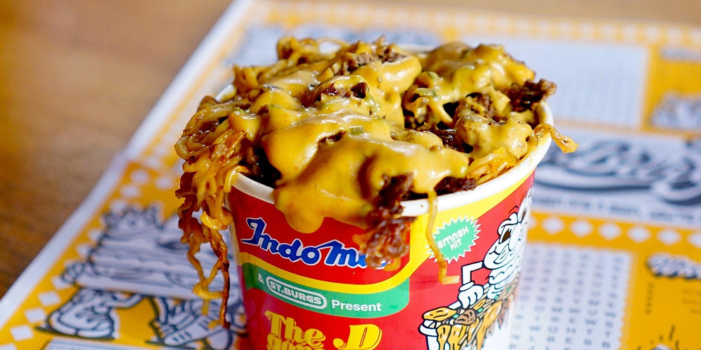 A close-up of St Burgs’ iconic D Goreng—a loaded bowl of instant Indomie noodles topped with smashed beef patties and molten American cheese. Served in a brightly branded St Burgs and Indomie collab container, this indulgent dish is one of Melbourne’s most outrageous limited-edition burger mashups, blending Filipino and Aussie comfort food with street-style energy.