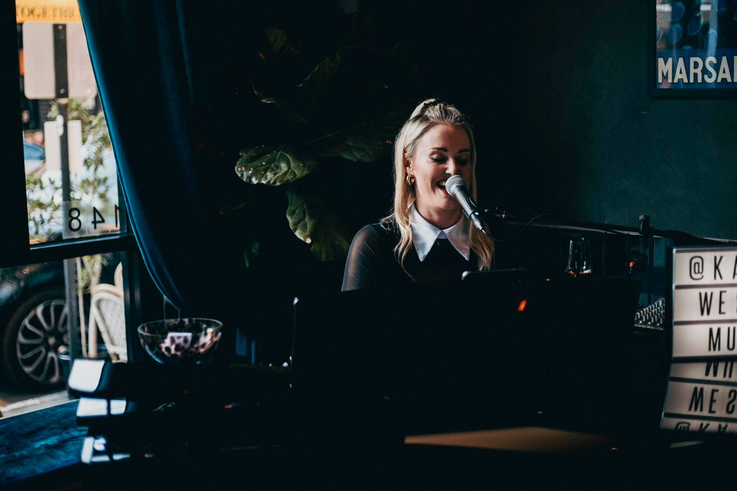 Live performer singing and playing piano at Ivy Piano Bar Windsor, a Chapel Street venue known for its live music, elegant cocktails and intimate ambience. The photo captures a blonde musician mid-performance beside a glass of wine and soft lighting, reflecting Melbourneβs vibrant nightlife and Ivyβs signature mix of sophistication and soul.